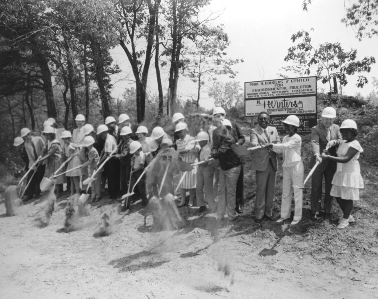 Various officials (including Mayor Hatcher) and children scooping shovelfuls of sand at the ground breaking of the Douglas Center.