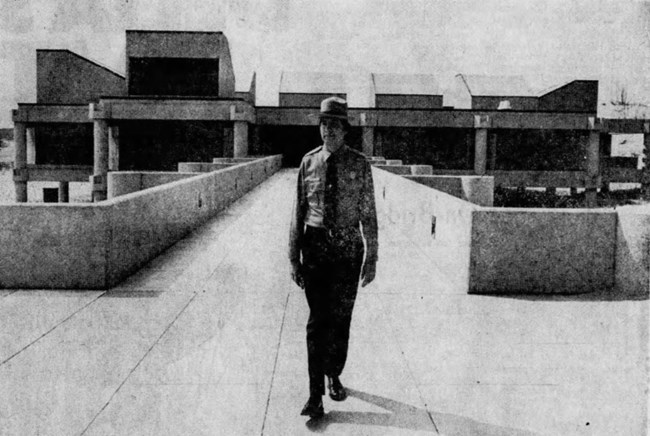 Black and white photograph of an NPS ranger standing in front of the newly constructed West Beach Bath House.