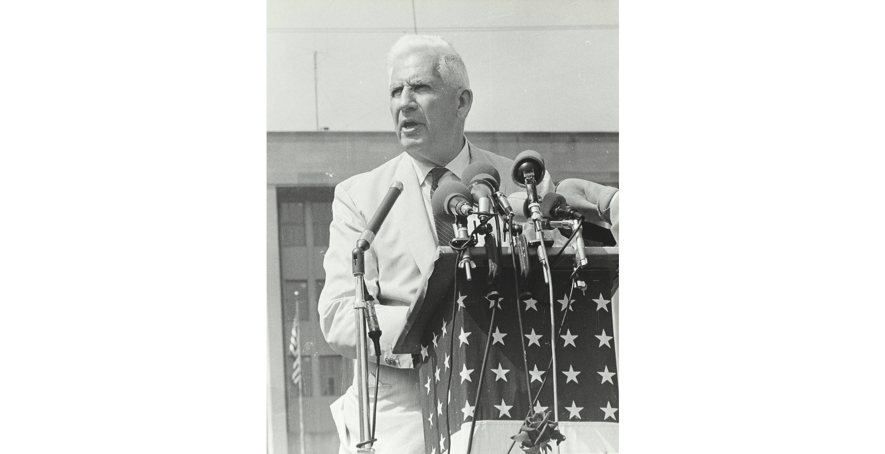 Black and white photograph of Senator Paul Douglas standing outside at a podium with an American flag