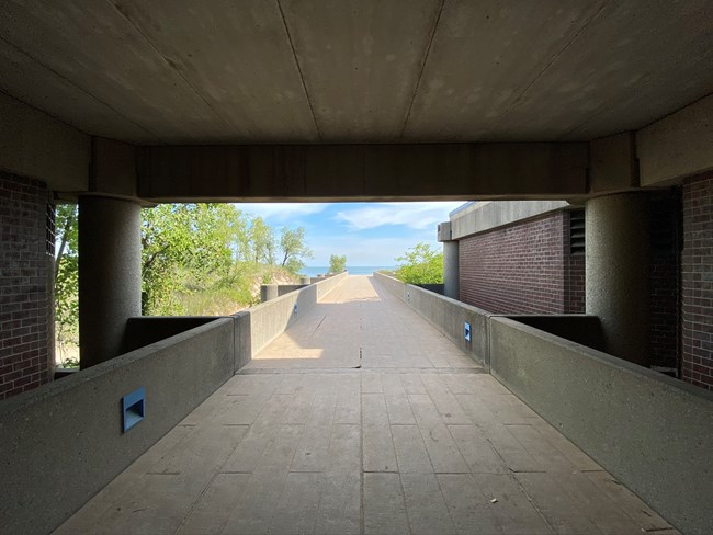 A concrete path extends to Lake Michigan as viewed from beneath an overhanging concrete ceiling.