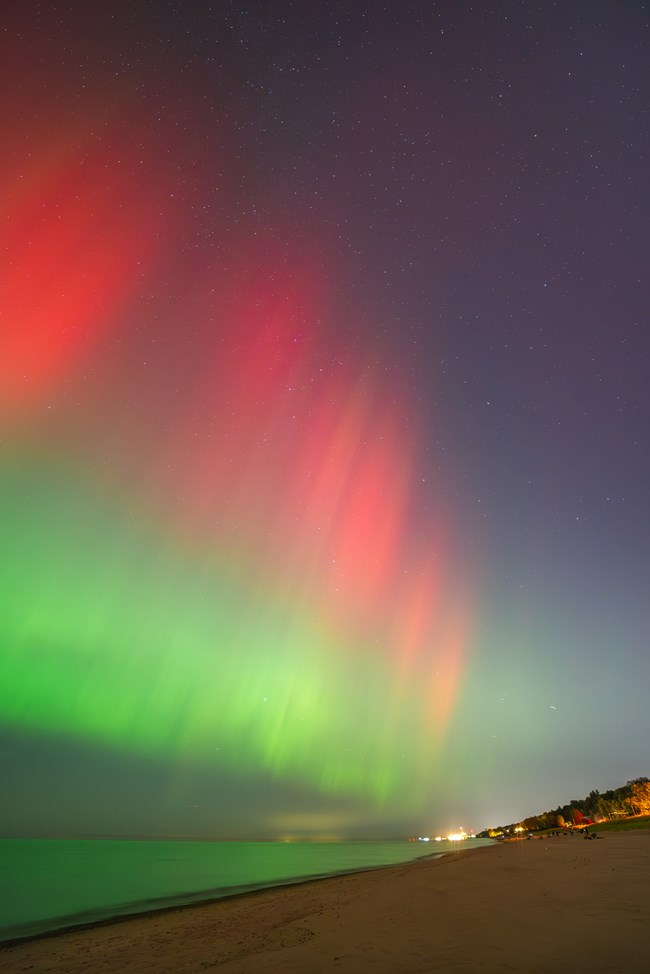 Red and green light fills the sky above Lake Michigan during aurora borealis