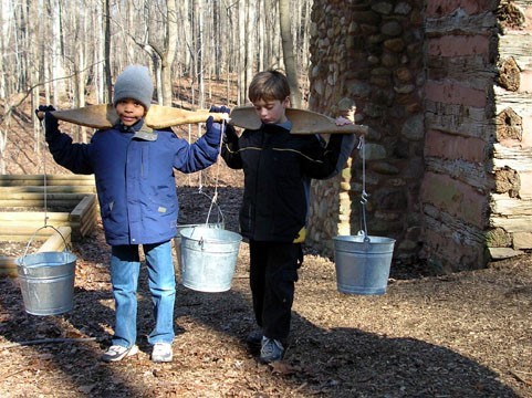 Two boys with yolks carrying sap buckets.