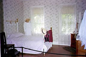bedroom with brass post bed with 2 large window on the wall beside it