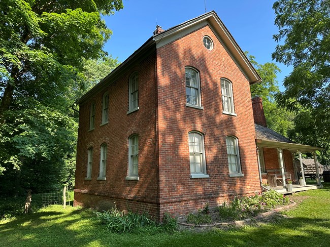 red brick farmhouse surrounded by green leafy trees and beneath a blue sky