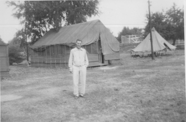 old black & white photo of camp director standing in front of tents