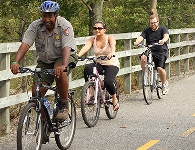 Ranger riding a bicycle with visitors along a paved bike trail.