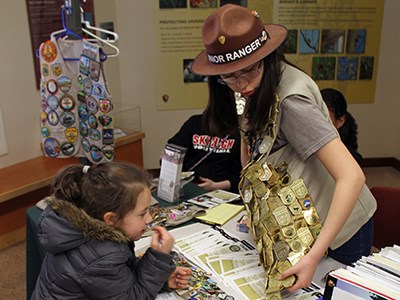 Volunteer with vest full of Junior Ranger badges helps young girl learn about the Junior Ranger program.