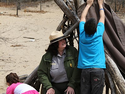 Ranger helps children build a fort out of driftwood and tree branches.