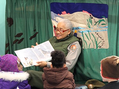 Ranger sitting on floor inside the Douglas Center reading a book to children.