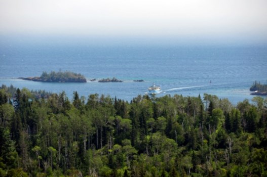 An aerial photo shows a large blue ferry entering a narrow rocky channel from open water