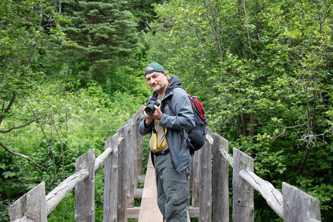 A person holding a camera with a large lens stands on a bridge and smiles for the photo.
