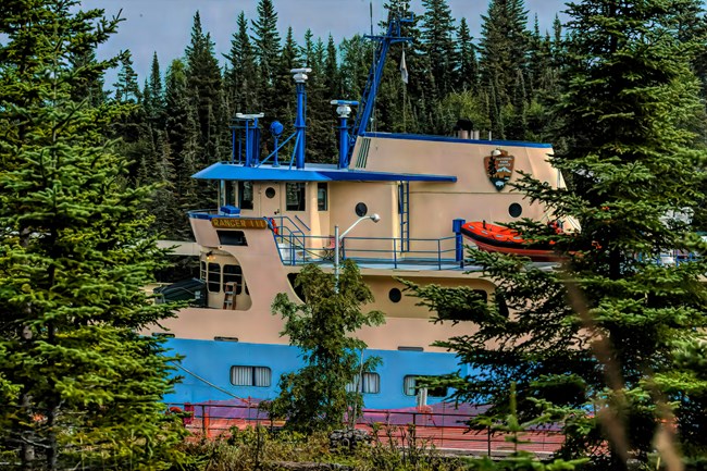A large blue and yellow ferry is visible through trees.