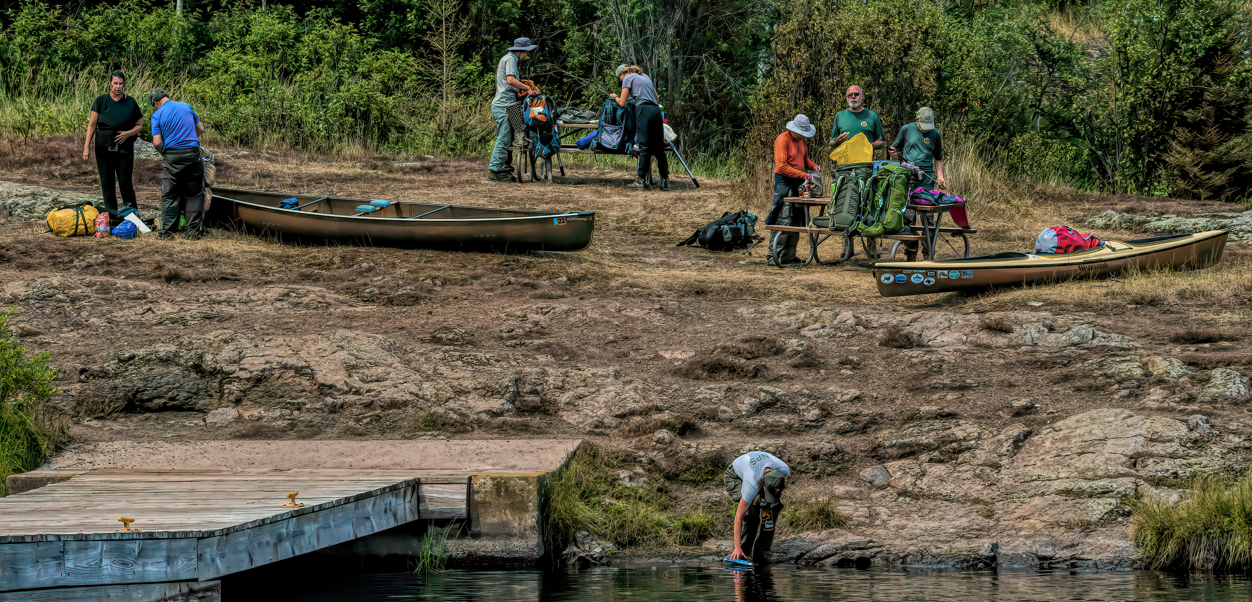 Multiple people near a dock completing tasks such as filtering water and moving a canoe.