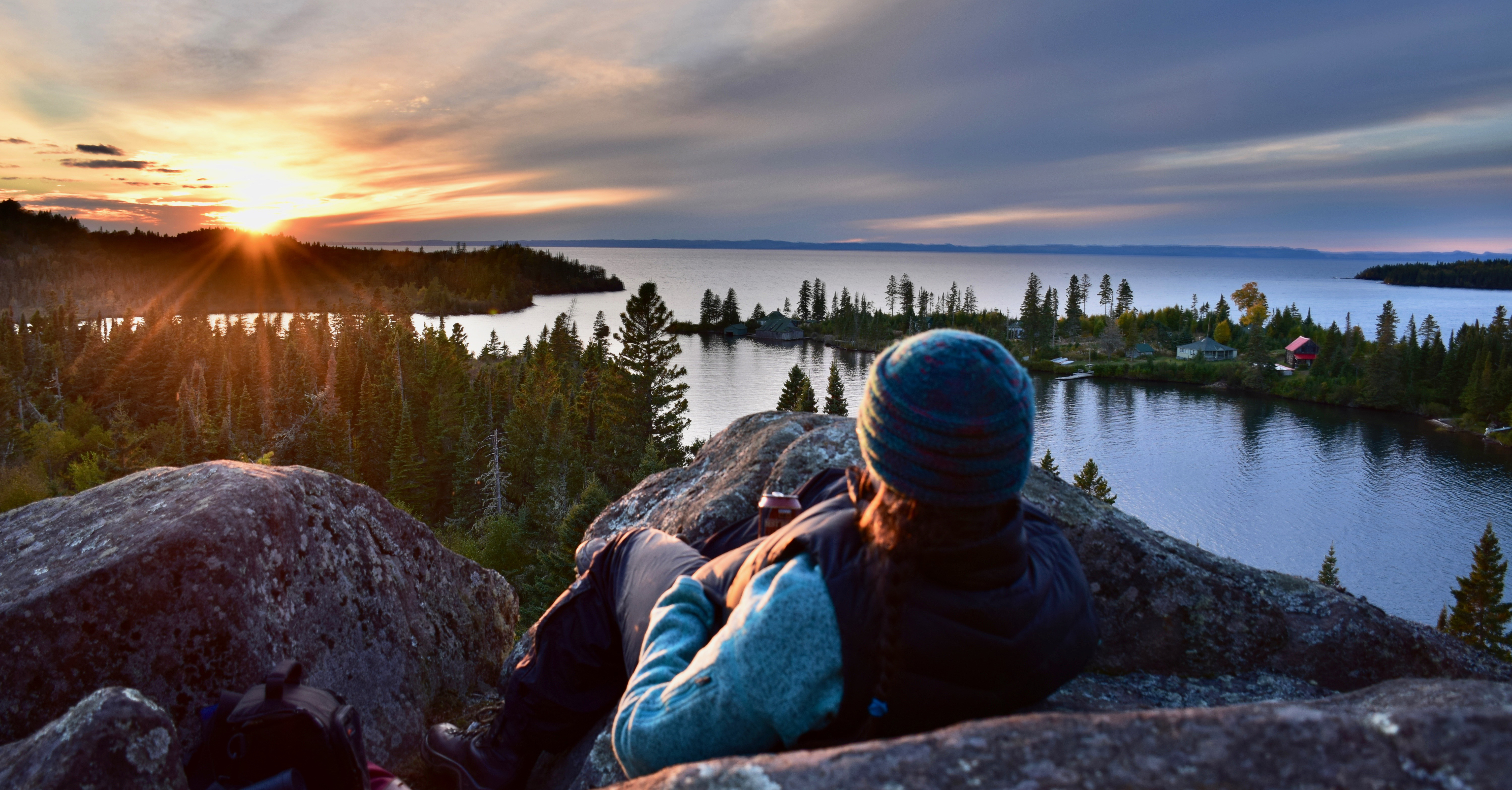 A person lays on a rock and view a sunset over an island and surrounding waters.