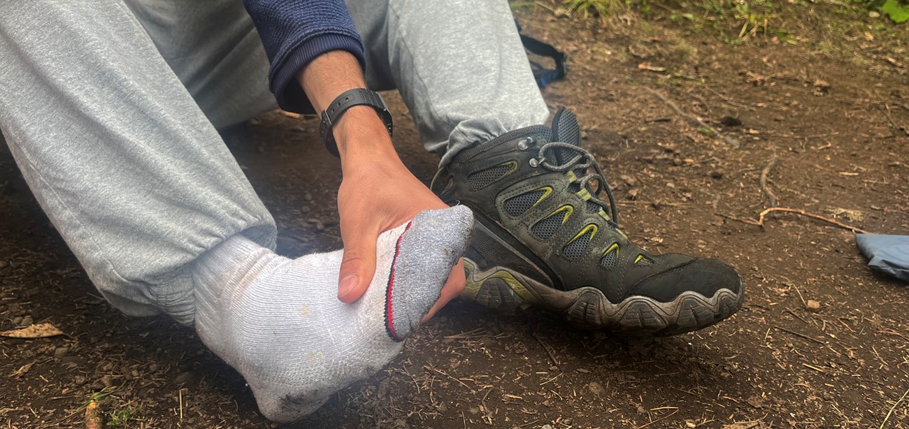 A person in hiking boots rubs their sore feet.
