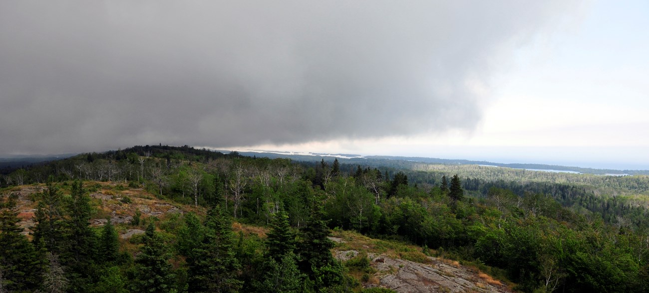 Dark storm clouds over a forested island ridge.