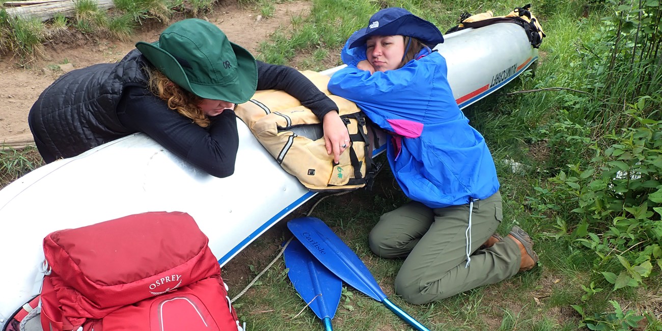Two tired people lay on a canoe.
