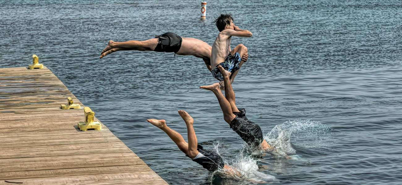 Three people dive off a dock into a lake.