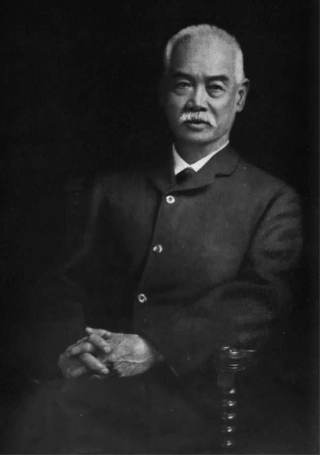 a chinese man sitting in a chair with hands folded in his lap