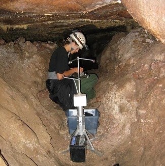 A caver is kneeling in a passageway, writing data into a small book.