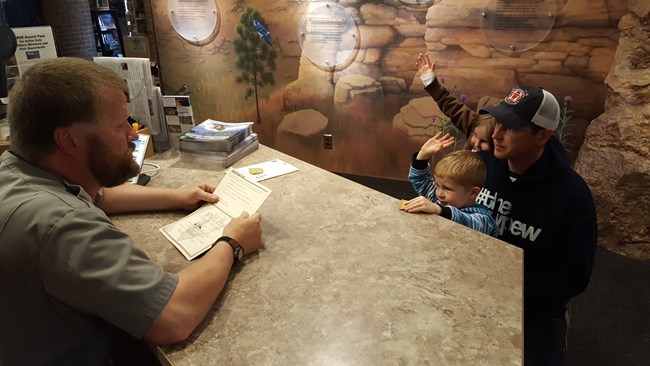 Junior Rangers taking an oath with Park Ranger Greg Hanson at the Jewel Cave visitor center front desk.