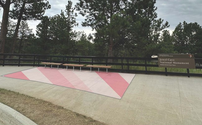 A concrete sidewalk with wooden benches next to a Jewel Cave National Monument sign. The area surrounding the benches is highlighted in red and white stripes.