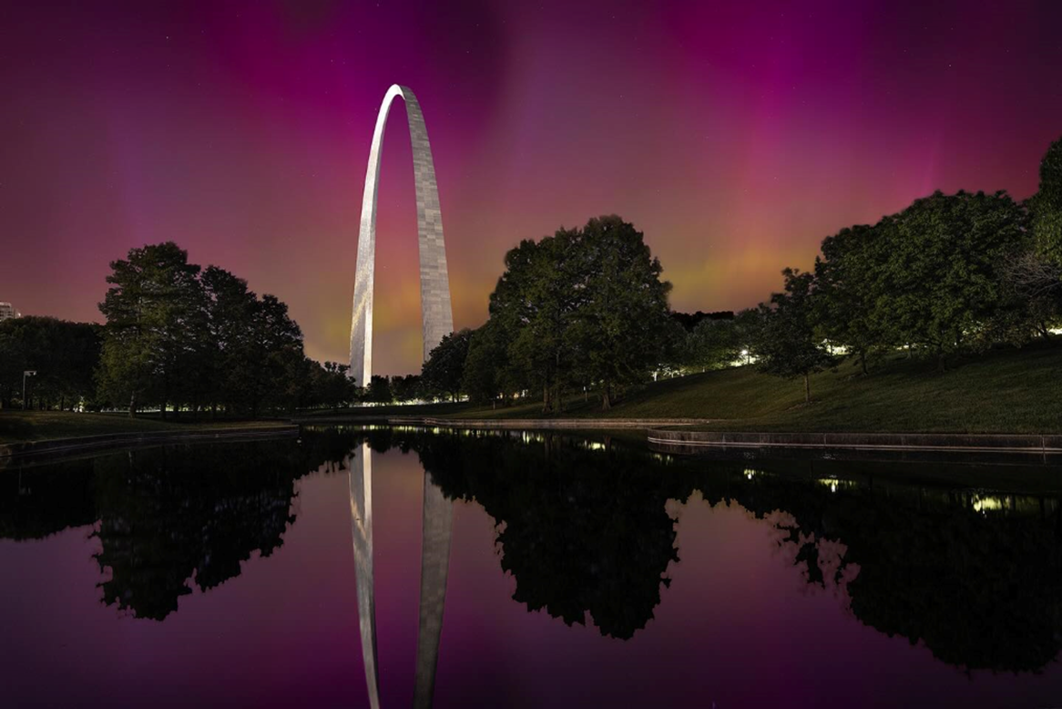 A silver-white arch, with a pink sky, reflected in water.