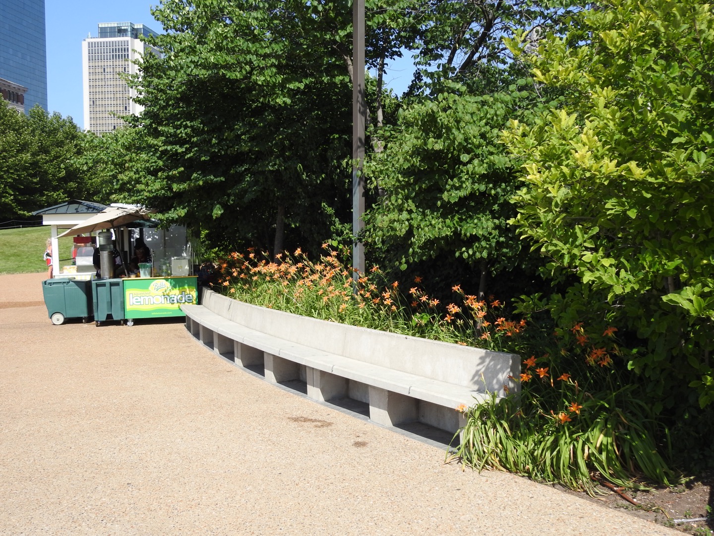 A row of orange flowers sticks out over a concrete bench. A lemonade stand is in the left-center of the photo.