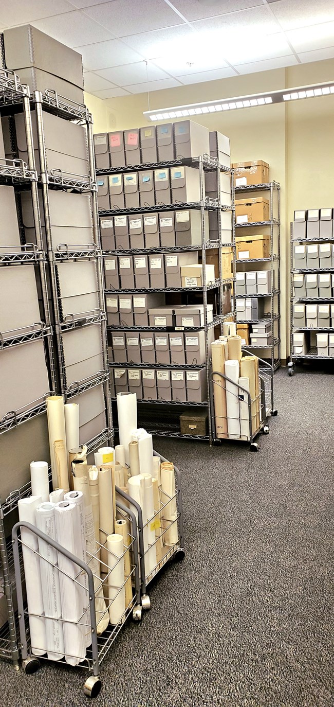 Section of room filled with rolled-up documents and shelves of gray archival boxes.