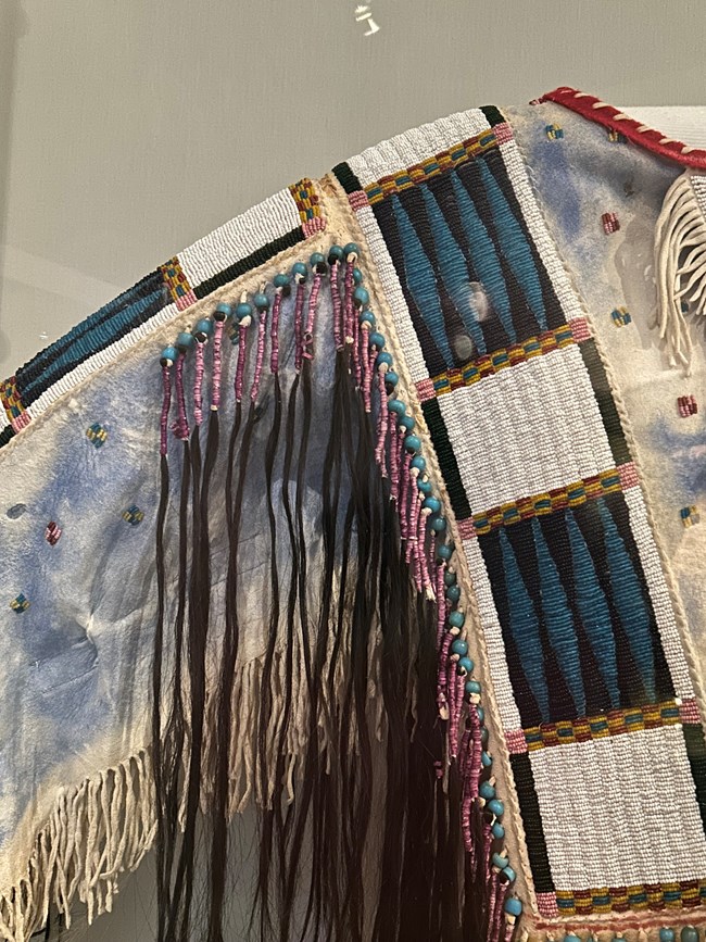 A closeup of the shirt shows the intricate beadwork and painting, as well as the quillwork and hair.