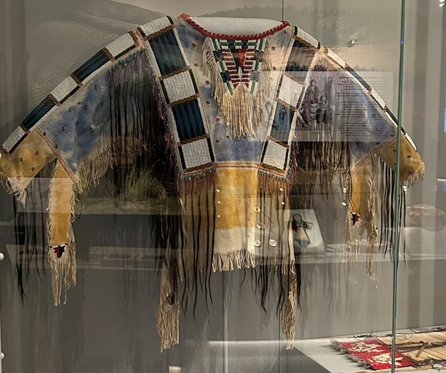 An intricately beaded and painted shirt behind glass at a museum