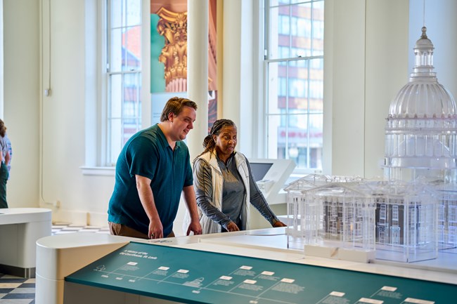 Two people look at a transparent model of a historic building in an exhibit gallery