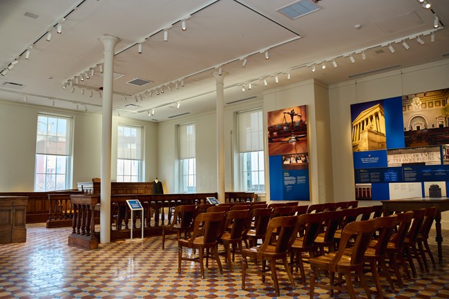 Rows of chairs and a judge's desk sit over a tiled floor