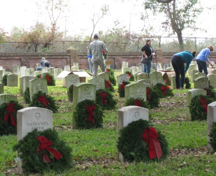 Image of people placing evergreen wreaths at headstones in Chalmette National Cemetery