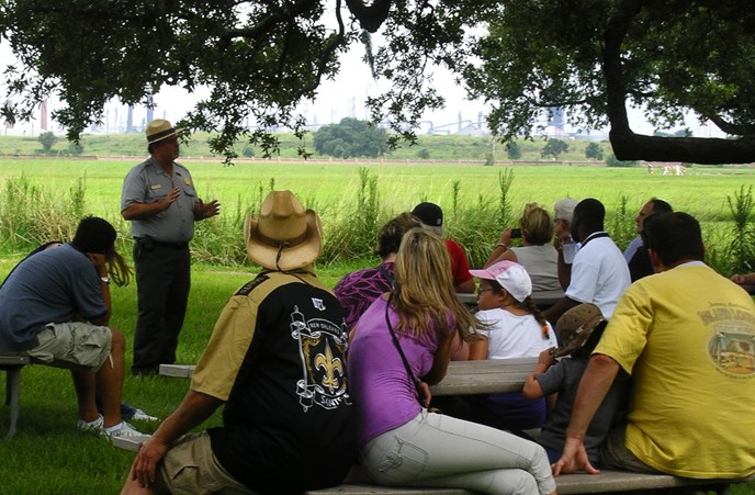 Image of park ranger talking to people seating at picnic tables under a tree's shade