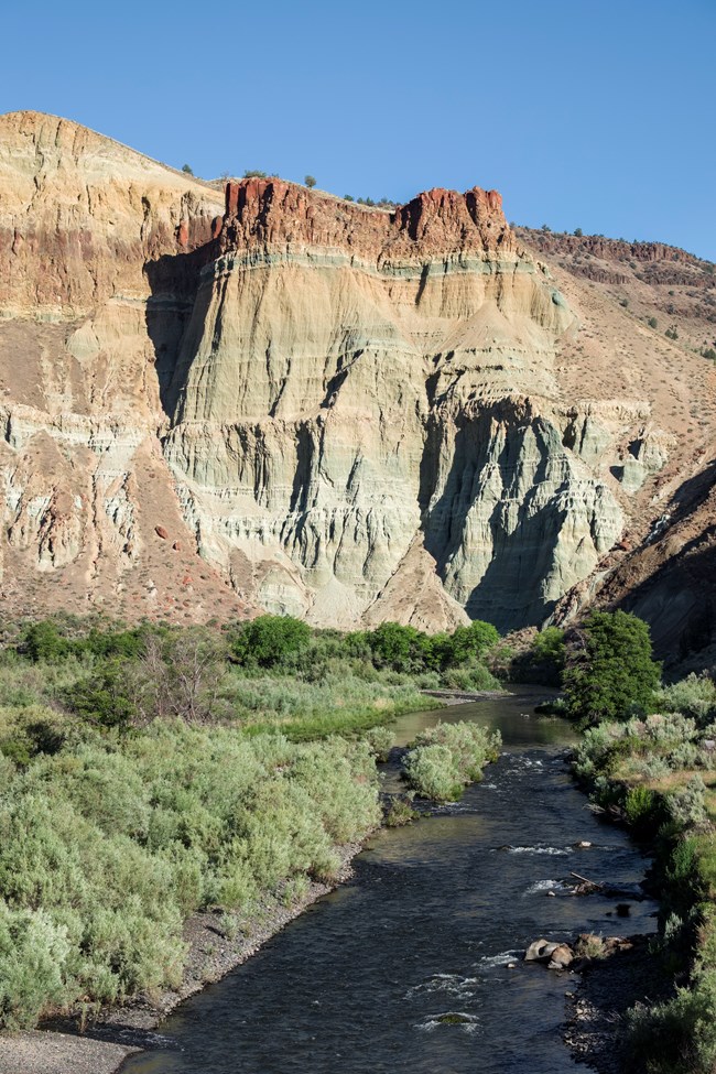 A rock outcrop with distinctive layers of harder rock and eroded layers that look like spires. A river flows below.