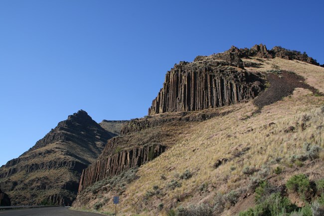 A hillside with outcroppings of columns of dark black basalt rock.