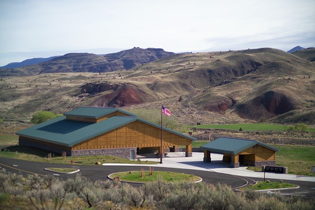 Brown wood building with green roof and a smaller outbuilding constructed the same. The American flag flies out front.