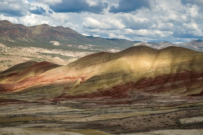 Striped tan and red hills in shadow with a band of sunlight lighting them up horizontally in the middle.