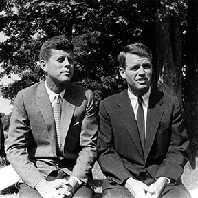 A black and white photo of John and Robert Kennedy in suits seated next to each other