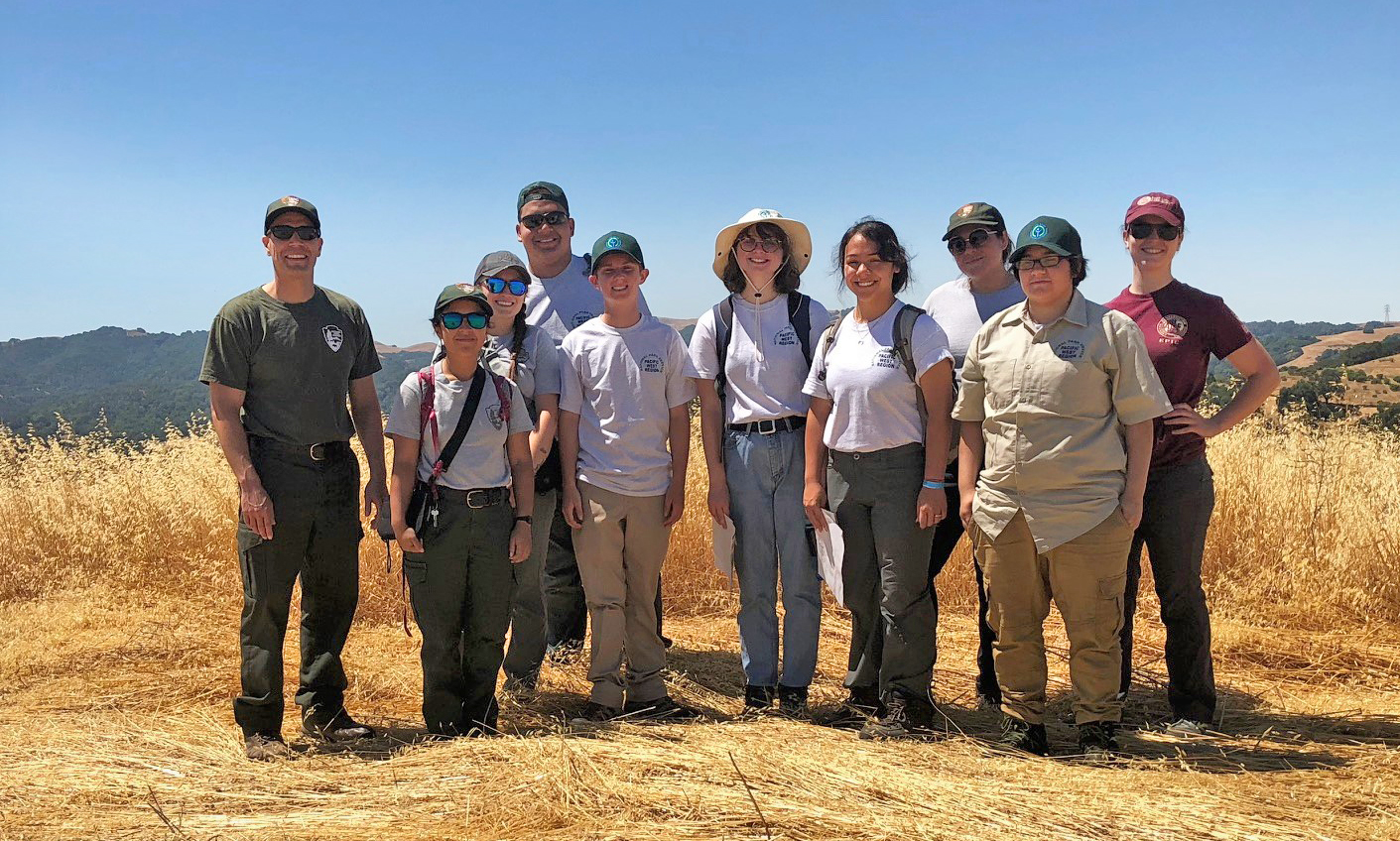 Multiple YCC crew youths pose for a photo on Mt. Wanda. Hills, yellow grass and a blue sky are seen.