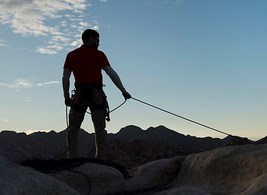 A belayer holding a rope at the top of a rock formation