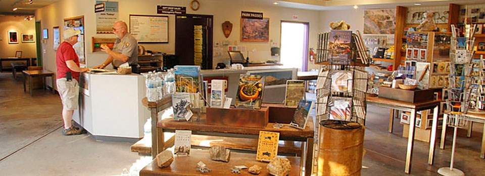 A park ranger speaks with a visitor surrounded by display cases in a bookstore and museum
