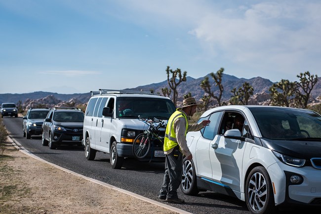 A person in a yellow vest talks to a person in a car.