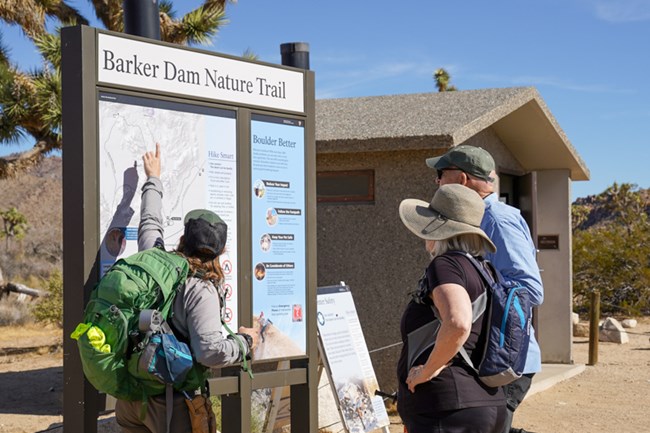 A park ranger points to a trailhead map next to visitors.