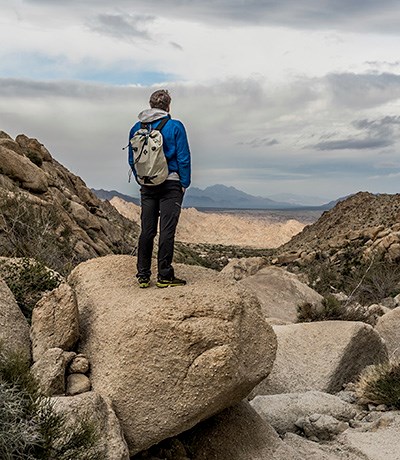 A hiker standing on a rock overlooking mountains and a valley.