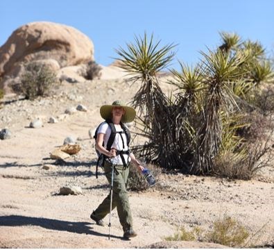 hiker on the trail in Joshua Tree with a yucca plant and boulder in the background