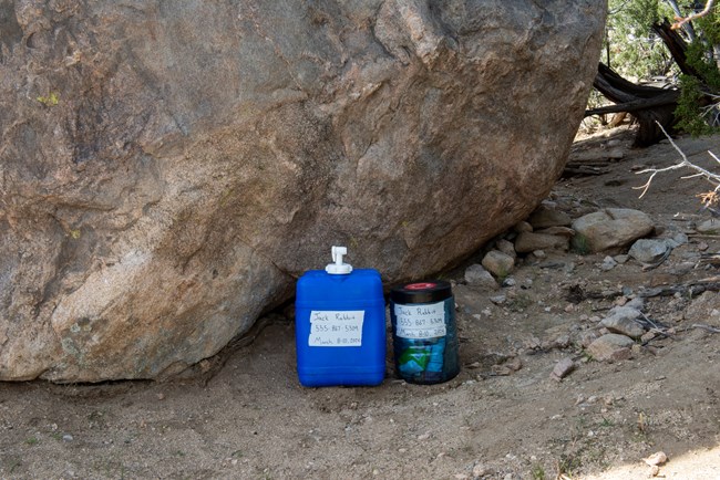 a water jug and platic canister next to a boulder