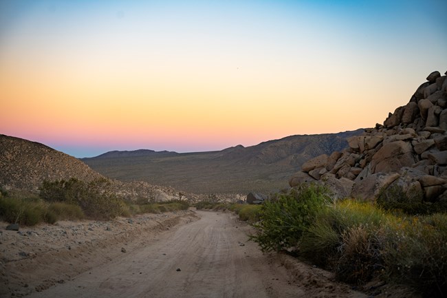 A dirt road winds off into a distant valley under a sunset sky.