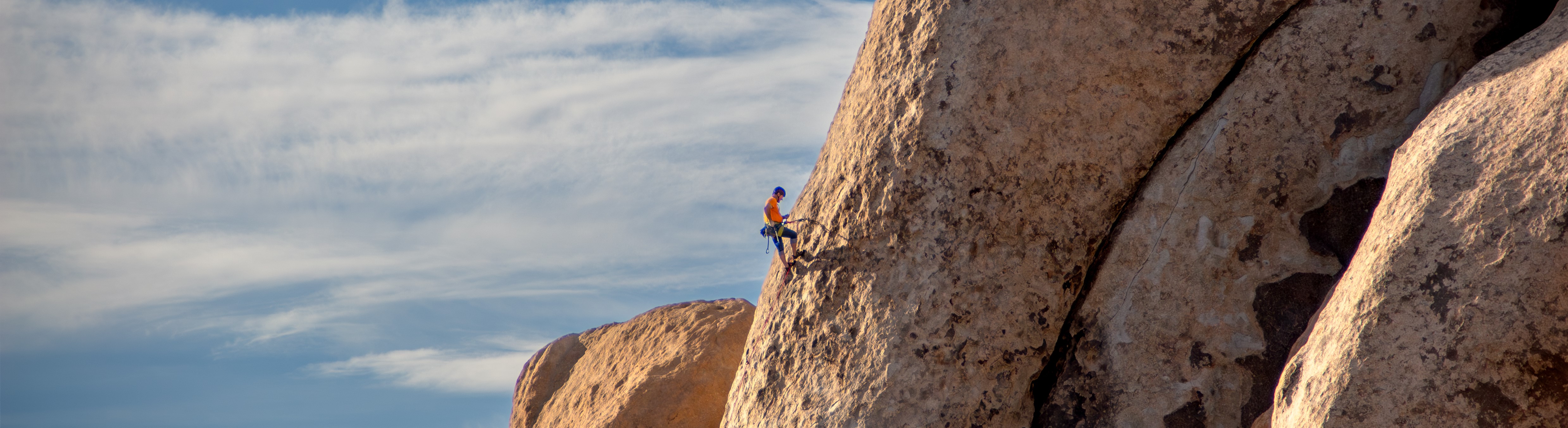 A climber in an orange shirt midway up a large boulder